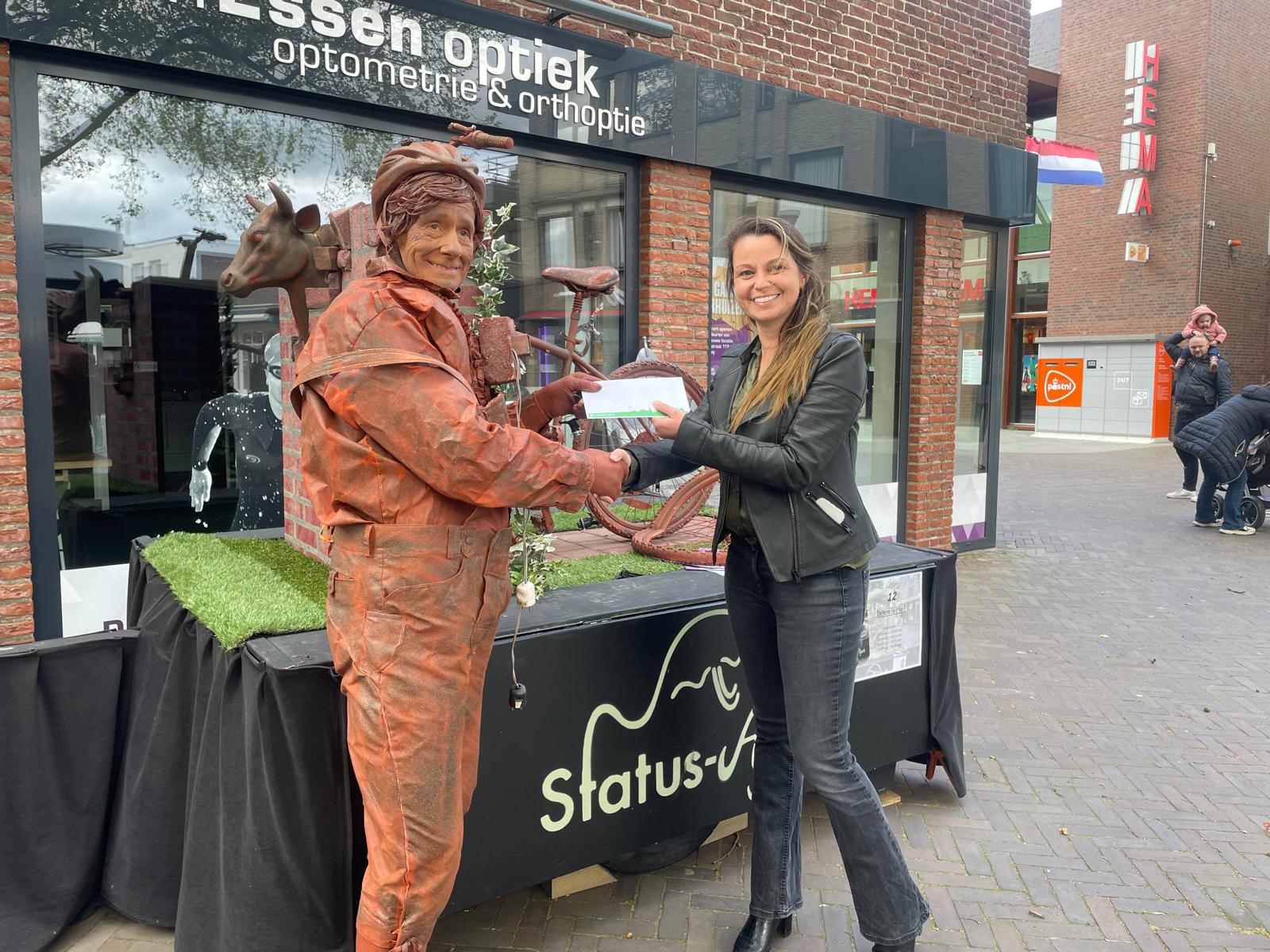 Mieke de Bruin ontvangt haar cadeaubon uit handen van het winnende Statue Boem is Ho