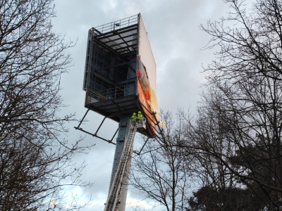 Brandweer met hoogwerker haalt doek vanreclamezuil